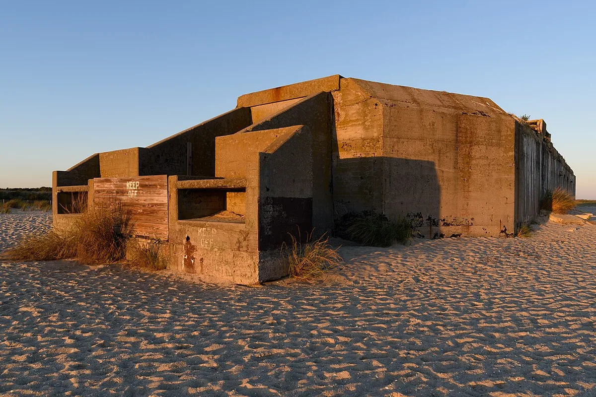 The concrete bulk of Battery 223 standing on the open beach at Cape May Point in low evening light, its gun embrasures facing the sea.