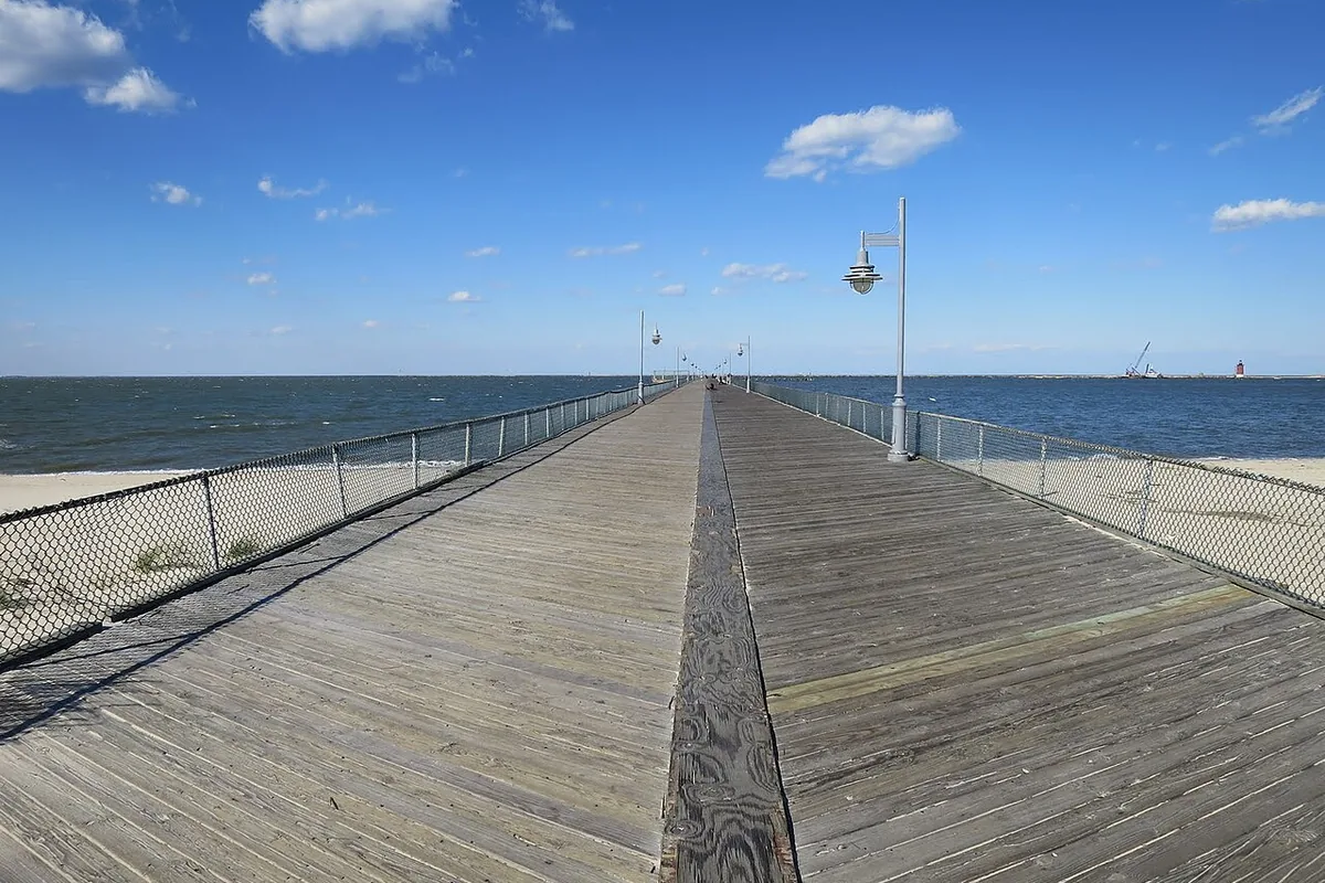 Looking along the wooden deck of the Cape Henlopen fishing pier towards Delaware Bay, with railings on both sides.