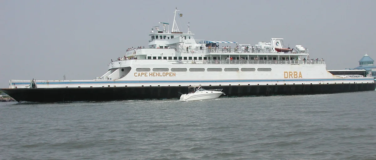 The Cape May-Lewes Ferry vessel MV Cape Henlopen under way off Cape May, New Jersey, in her cream and gold 1980s livery, with a small motorboat crossing in front of her.