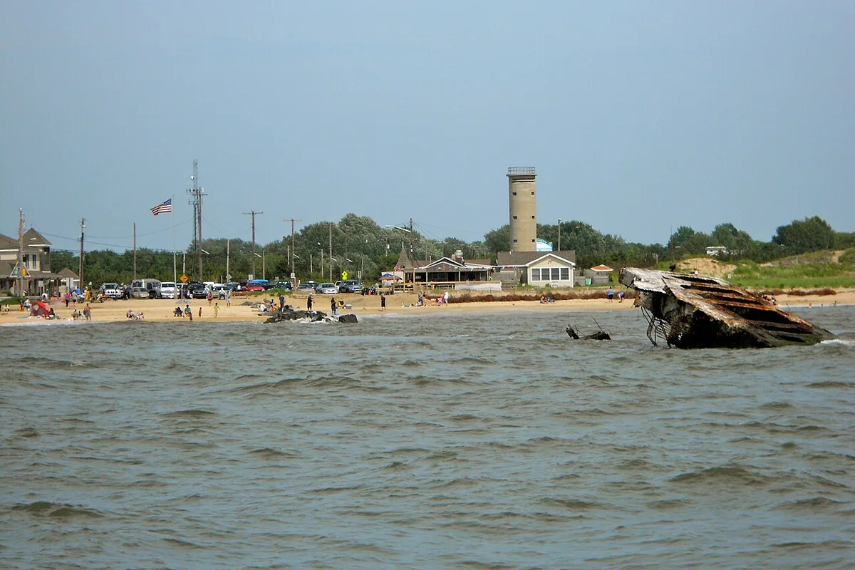 Sunset Beach at Cape May Point seen from Delaware Bay, with bathers on the sand, the gift shop buildings, Fire Control Tower 23 and the wreck of the Atlantus.