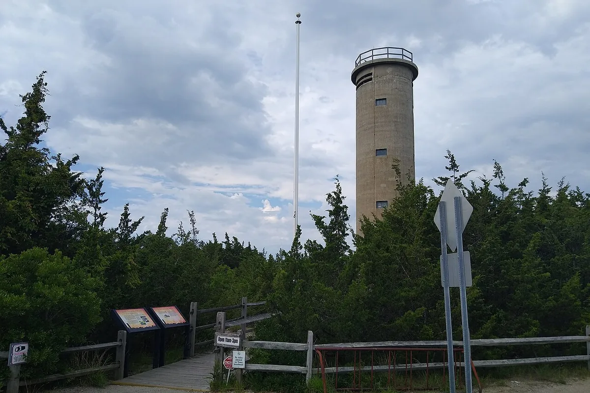 Fire Control Tower No. 23 at Sunset Beach, Cape May Point, seen from its entrance path with interpretive signs in the foreground.